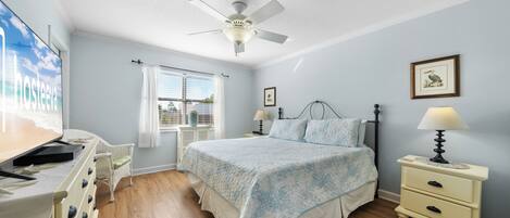 A bedroom with a bed, bedside tables, a ceiling fan, a window with blinds, and a wall-mounted TV.