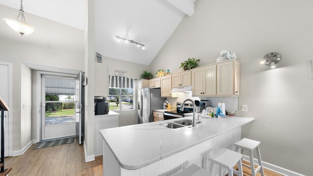 Una cocina moderna con armarios blancos, una isla central con taburetes y vistas al exterior a través de un ventanal.
