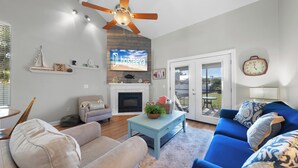Una sala de estar con chimenea, ventilador de techo, televisión y comedor.