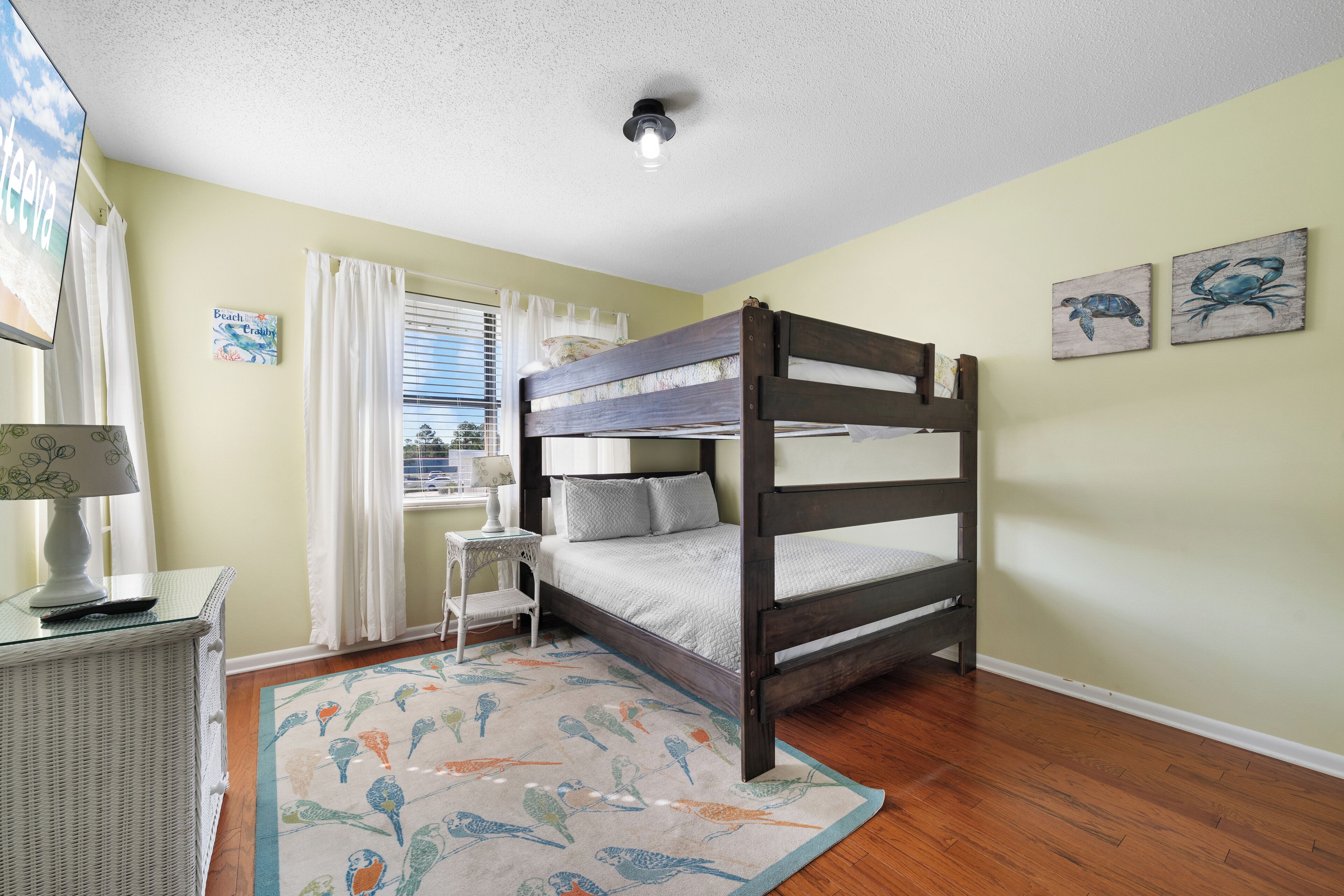 Un dormitorio con una cama litera, una mesita con lámpara, una ventana con cortinas y decoración en la pared.