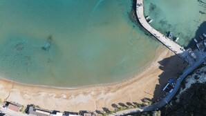 An aerial view of a coastal area with a curved road, clear turquoise waters, and a sandy beach.