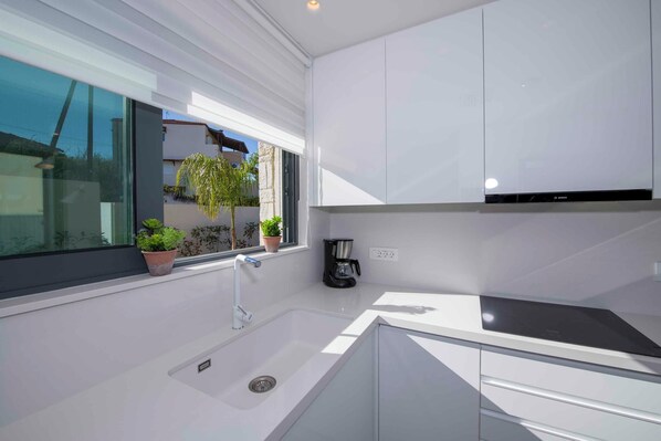 Una cocina moderna con armarios blancos, un lavamanos integrado y un ventanal con vistas a un jardín.