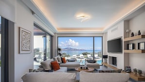 A modern living room with a large TV, comfortable seating, a pool view, and a mountain in the background.