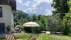 Ein Garten mit zwei gestreiften Stühlen, einem Tisch, einem Holzzaun und einem weißen Sonnenschirm.