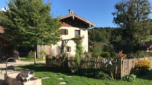 Ein rustikales Haus mit Holzzaun, ein Garten mit einer Steinfontäne und einer Katze auf einem Steinsims.