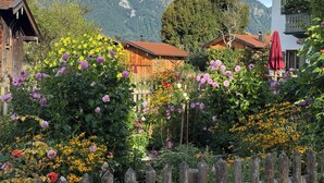 Ein rustikaler Garten mit Holzhäusern, einem Holzzaun und einer Bergkulisse.