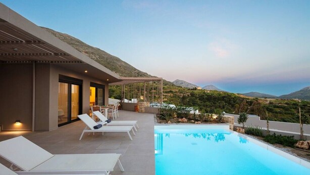 Eine moderne Villa mit Pool, Sitzgelegenheiten im Freien und Blick auf die umliegenden Hügel.