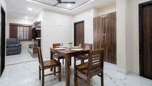 Un coin repas avec une table et des chaises en bois, un ventilateur de plafond et un téléviseur fixé au mur.