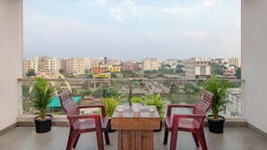 Un balcon avec une table en bois et deux chaises, des plantes en pot et une vue sur un paysage urbain avec des bâtiments et un pont.