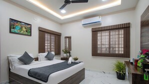 Une chambre moderne avec un grand lit, deux fenêtres équipées de stores, un climatiseur et un ventilateur de plafond.