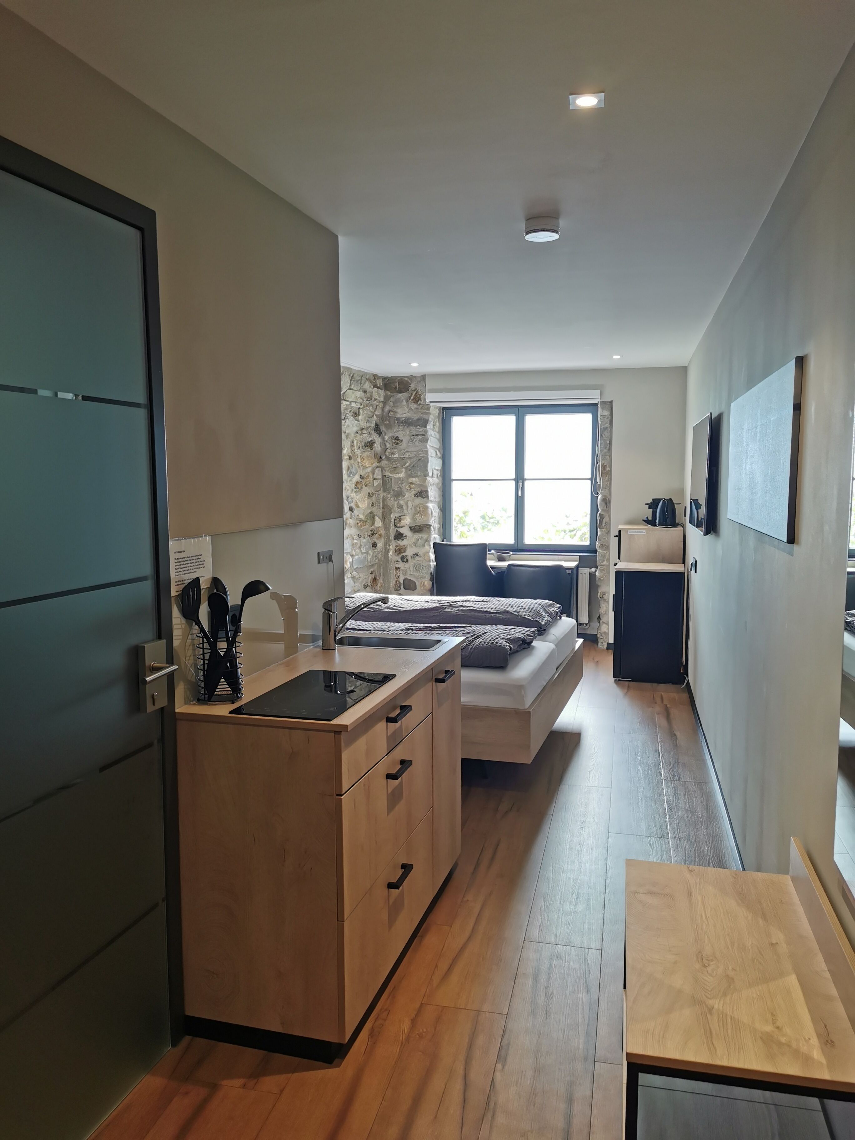 A modern kitchen with a built-in stove, wooden cabinets, and a window overlooking a garden.