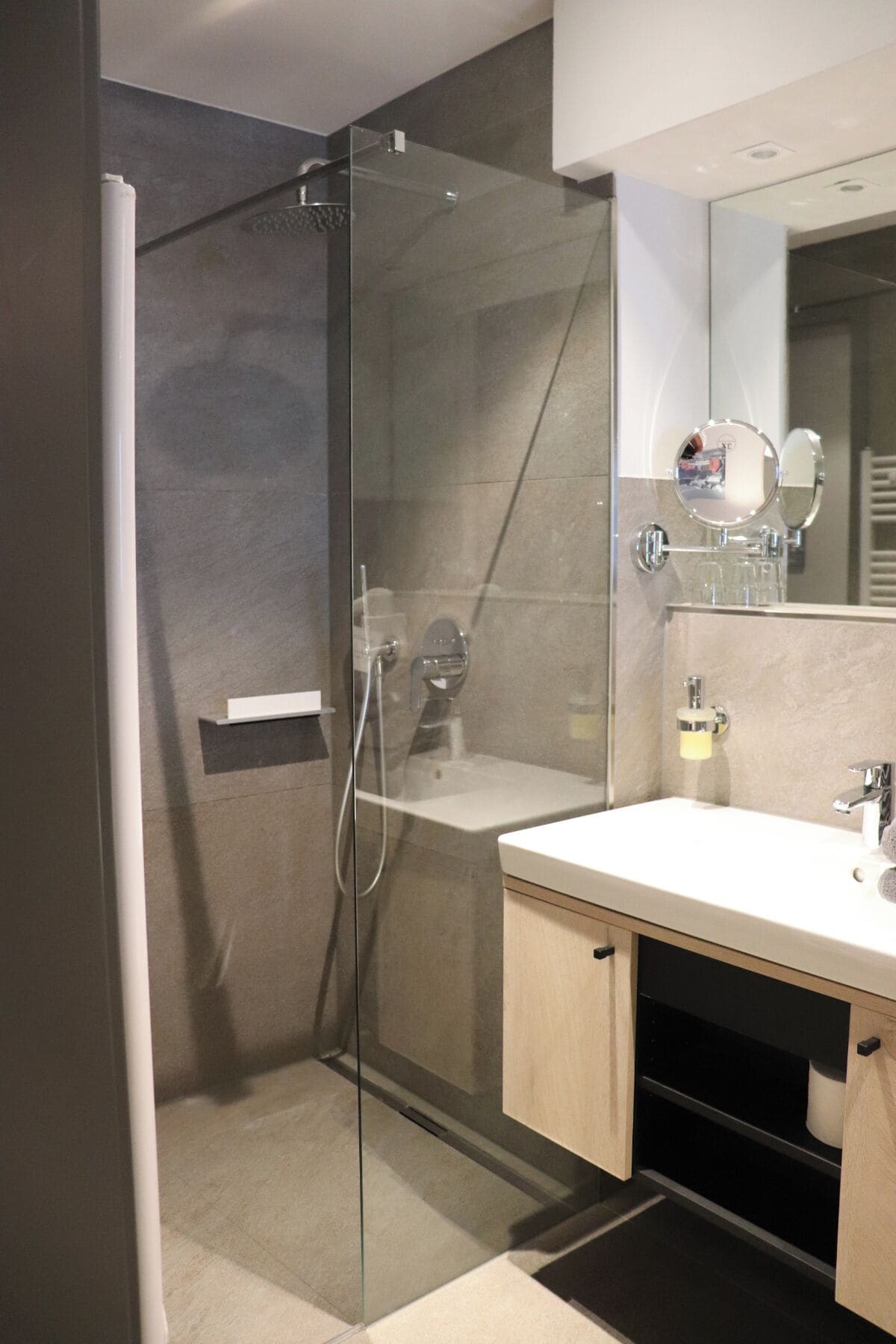 Un baño moderno con ducha envuelta en vidrio, un lavamanos blanco con espejo y un armario de madera.