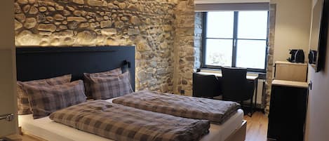 Un dormitorio con pared de piedra, cama con ropa de cama escocesa, escritorio con silla y ventana.