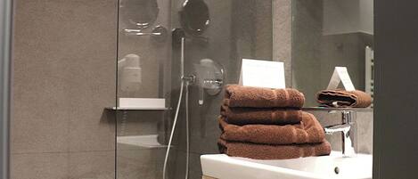 A modern bathroom with a glass shower enclosure, a vanity with a mirror, and a stack of towels.
