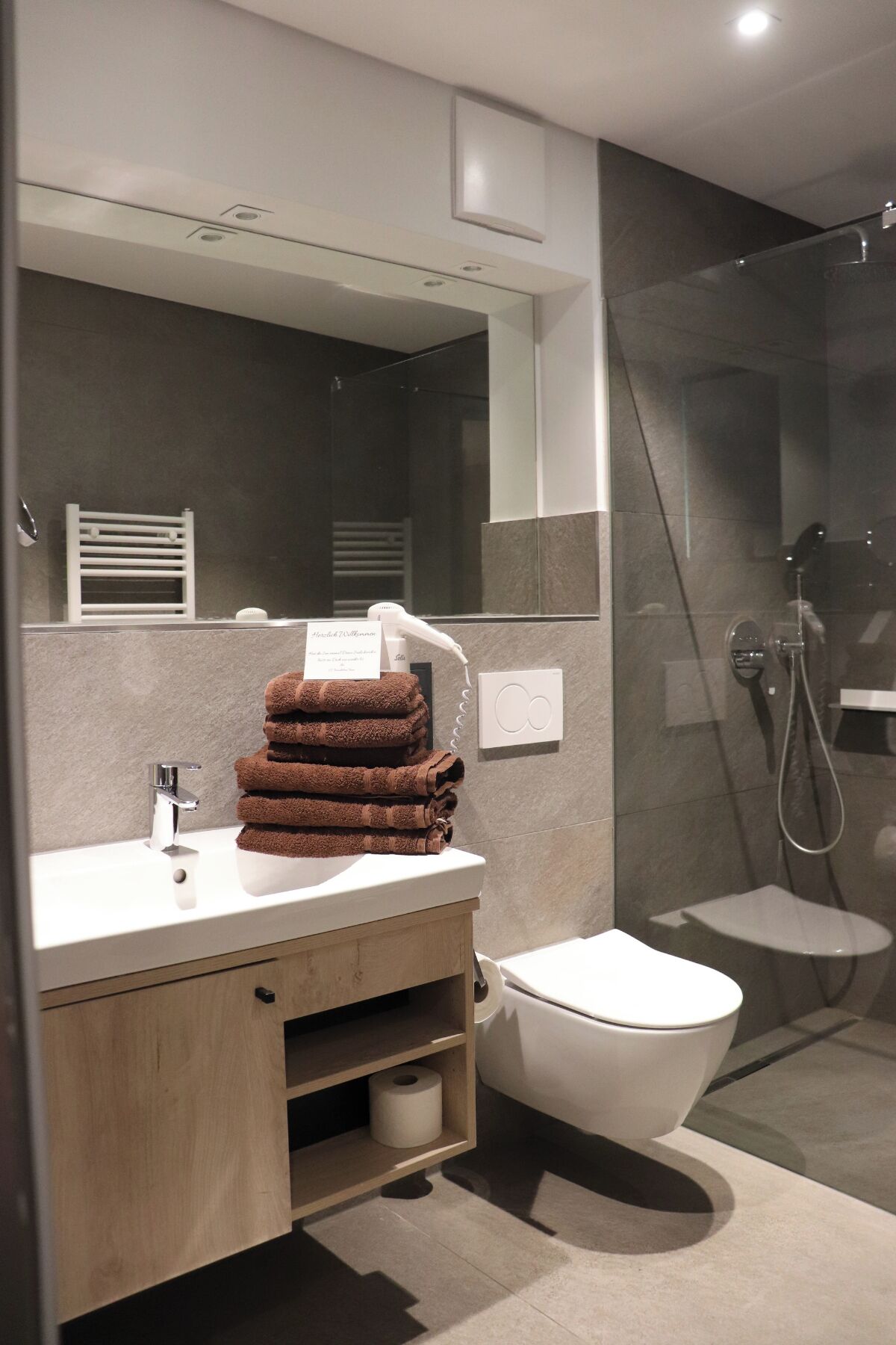 Une salle de bain moderne avec un lavabo blanc, un porte-serviettes, des toilettes et une douche séparée par une paroi de verre.