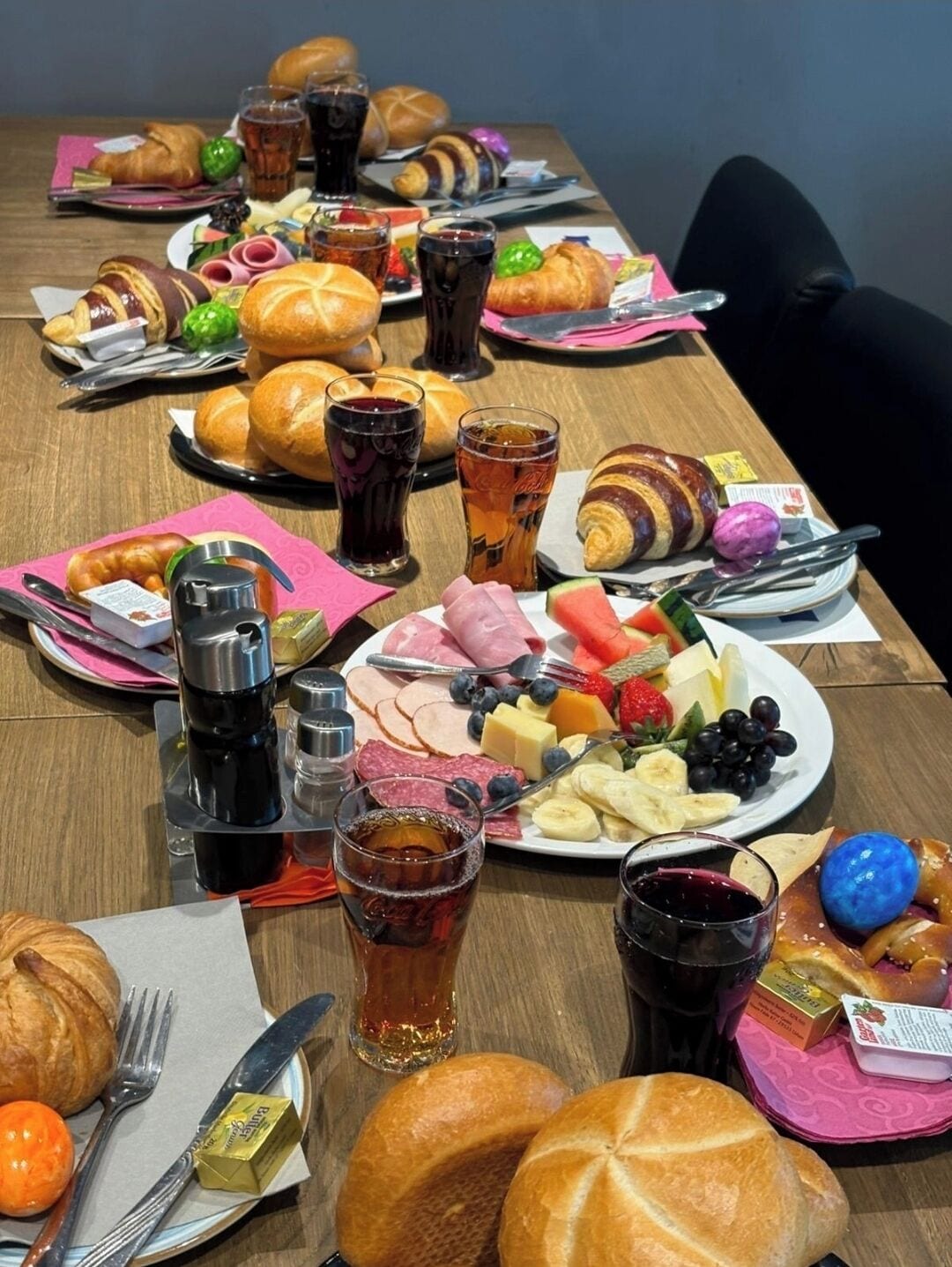 Ein Tisch ist reichhaltig mit Frühstücksleckereien wie Croissants, Käse, Obst und Getränken gedeckt.