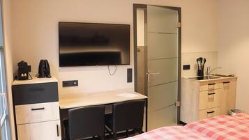 Habitación de hotel con cama, escritorio, dos sillas, televisor, minibar, armario y baño.