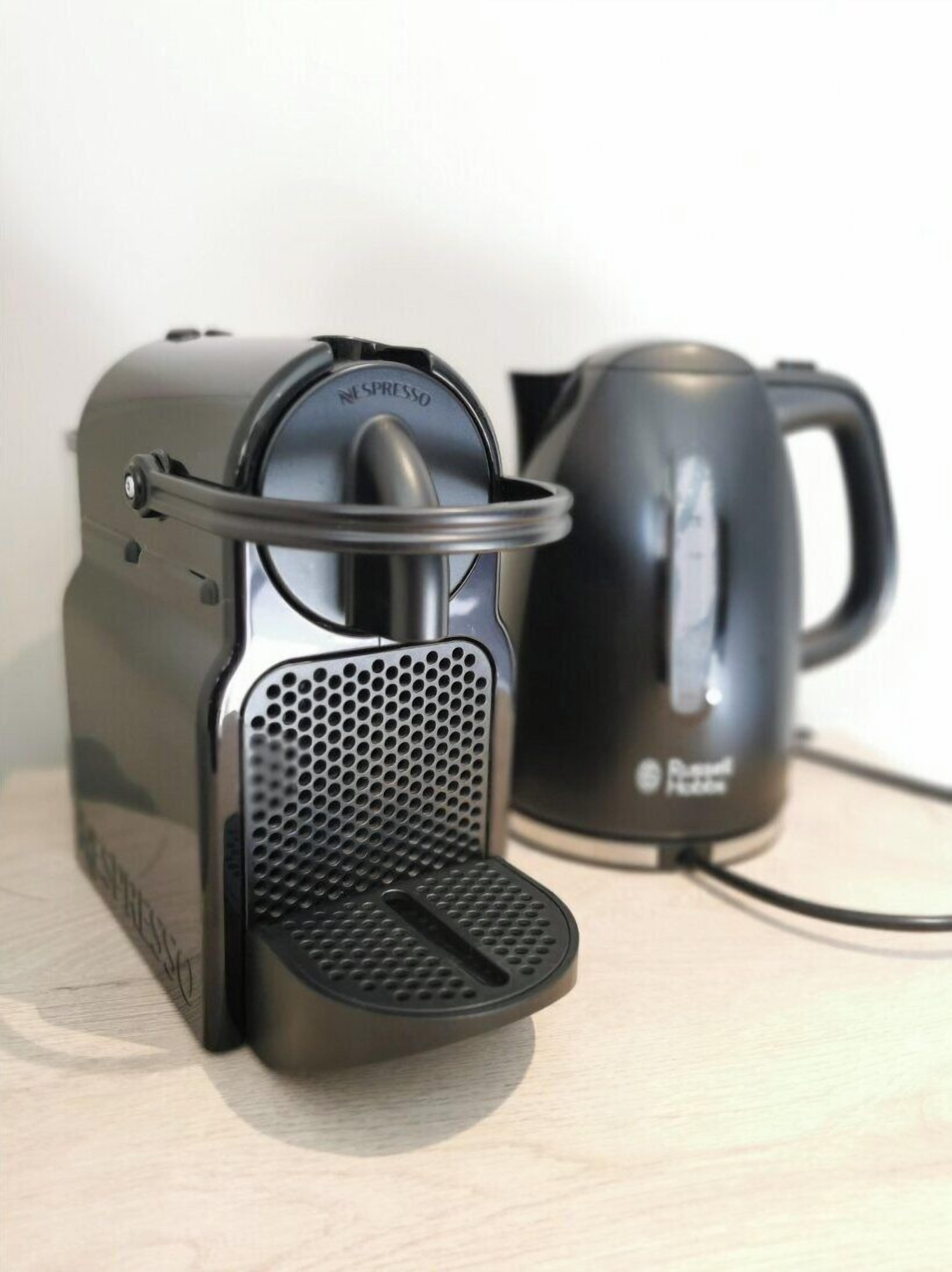 A Nespresso coffee machine with a black and silver design, a kettle, and a power cord on a wooden surface.