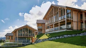Un edificio moderno de madera con ventanas grandes y balcones, ubicado en una ladera cubierta de césped.