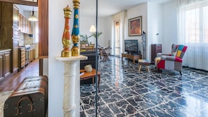 A spacious living room with a marble floor, wooden cabinets, a television, and a colorful armchair.