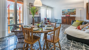 A dining area with a round table, wooden chairs, a vase with green plants, and a hanging light fixture.