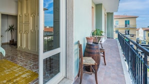 A balcony with a view of neighboring buildings, a wooden chair, a potted plant, and a large cabinet.