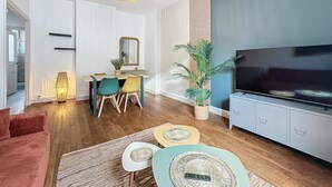 Un salon moderne doté d’un téléviseur à écran plat, d’un coin repas avec une table et des chaises, et d’une grande plante en pot.