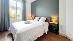 Une chambre avec un grand lit, deux tables de chevet avec des lampes, une fenêtre avec des rideaux et une vue sur la verdure à l’extérieur.