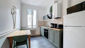 A compact kitchen with a wooden table, a green chair, a built-in microwave, and a white refrigerator.