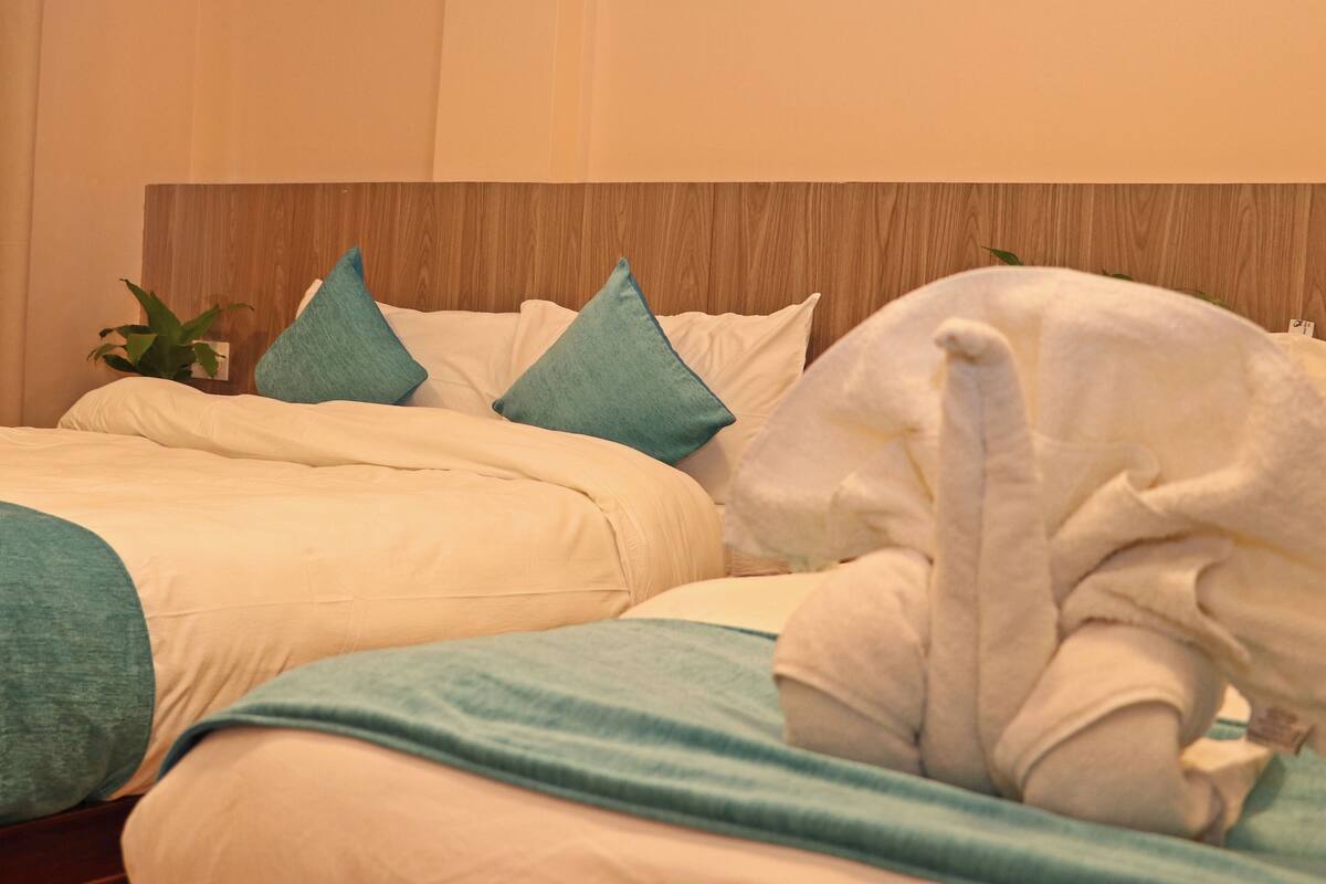 A hotel room with a wooden headboard, a bed with white and teal bedding, and a white towel on the bed.