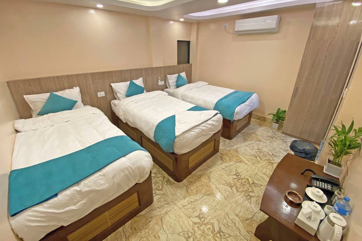 A hotel room with three beds, a wooden headboard, a marble floor, a small table with toiletries, and an air conditioning unit on the wall.