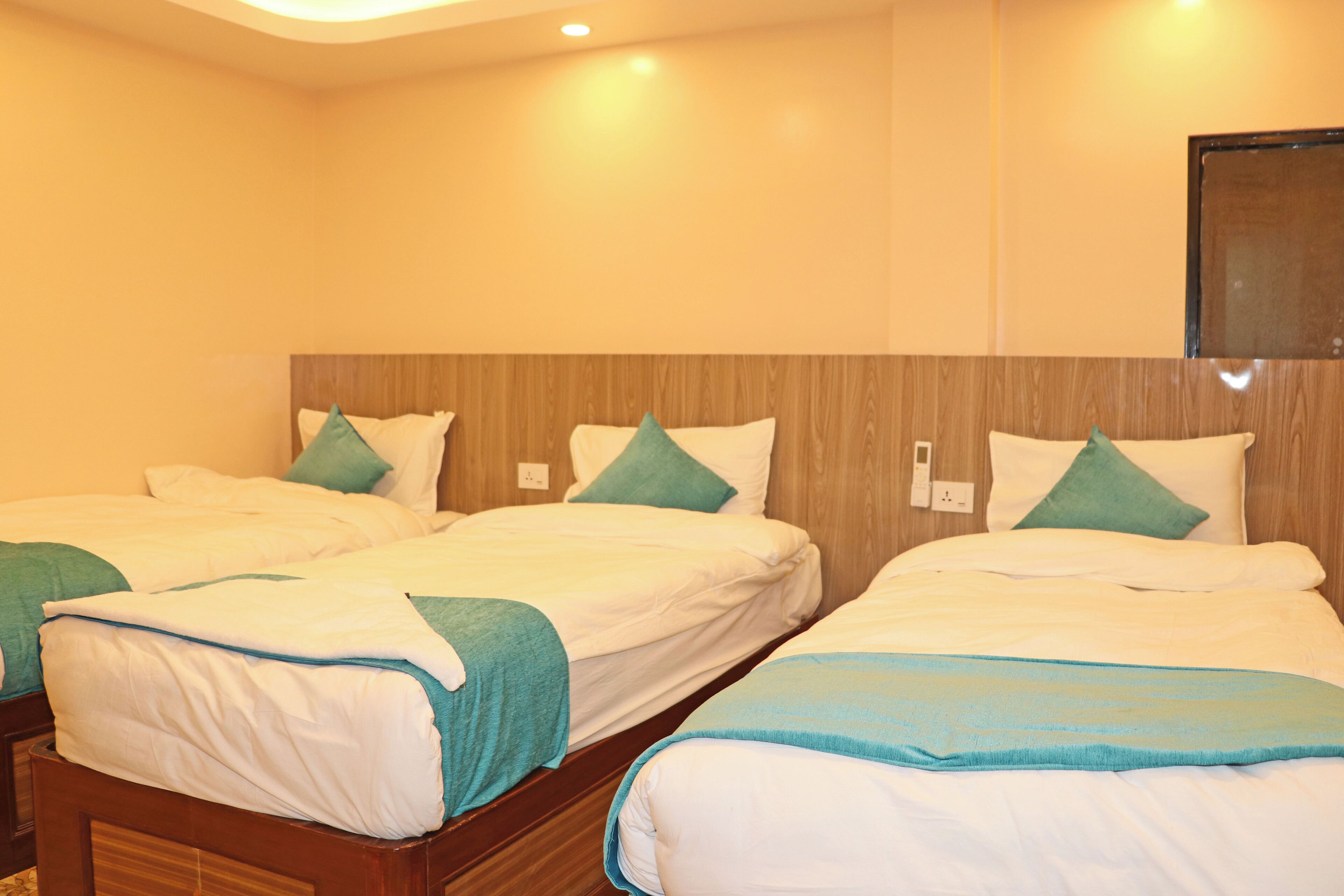 A hotel room with three beds, each with white bedding and teal accents.