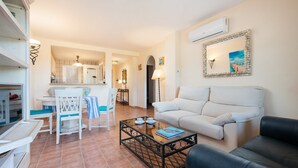 A living room with a white sofa, a black leather couch, a coffee table, and a dining area with a white table and chairs. - The Torrent's Observer Holiday Home - Apartment (Cala Pi, Illes Balears)