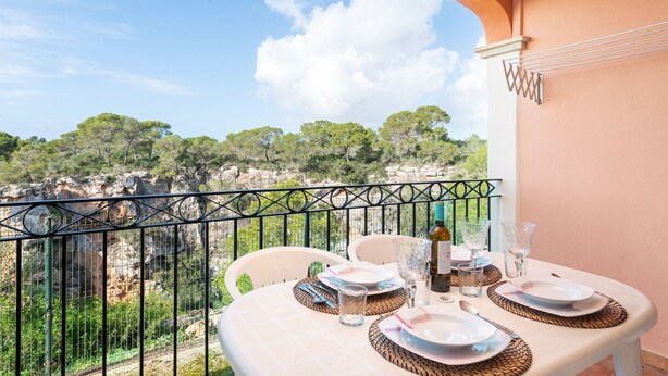 A balcony with a table set for dining, overlooking a rocky landscape with trees. - The Torrent's Observer Holiday Home - Apartment (Cala Pi, Illes Balears)