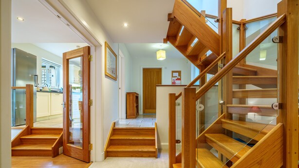 A modern interior with wooden stairs leading to a second floor, a kitchen area, and a visible door to another room.