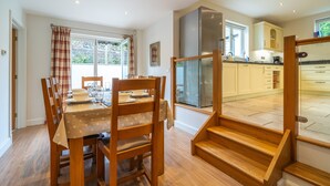 A dining area with a wooden table and chairs, a kitchen with white cabinets, and a staircase leading to an upper floor.