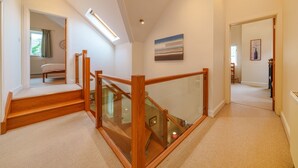 A modern interior with a wooden staircase, glass railing, and a view of a bedroom.