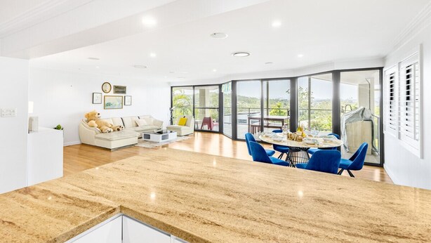 Amplia sala de estar con cocina, comedor y grandes ventanales que ofrecen vistas al exterior.