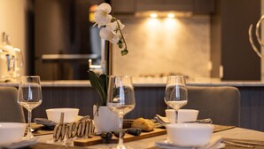 Una mesa de comedor dispuesta con vajilla blanca, un florero con flores blancas y una tabla de madera con alimentos.