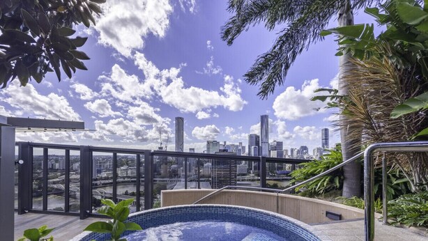 Una piscina en la azotea con vistas a la ciudad, rodeada de vegetación y arquitectura moderna.