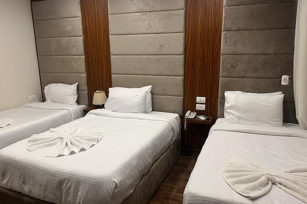 Hotellihuoneessa on kolme sänkyä, joissa kaikissa on valkoiset vuodevaatteet ja pyyhe. Sängyn päädyssä on puinen koristepaneeli, yöpöydällä on lamppu ja huoneessa on myös puhelin.