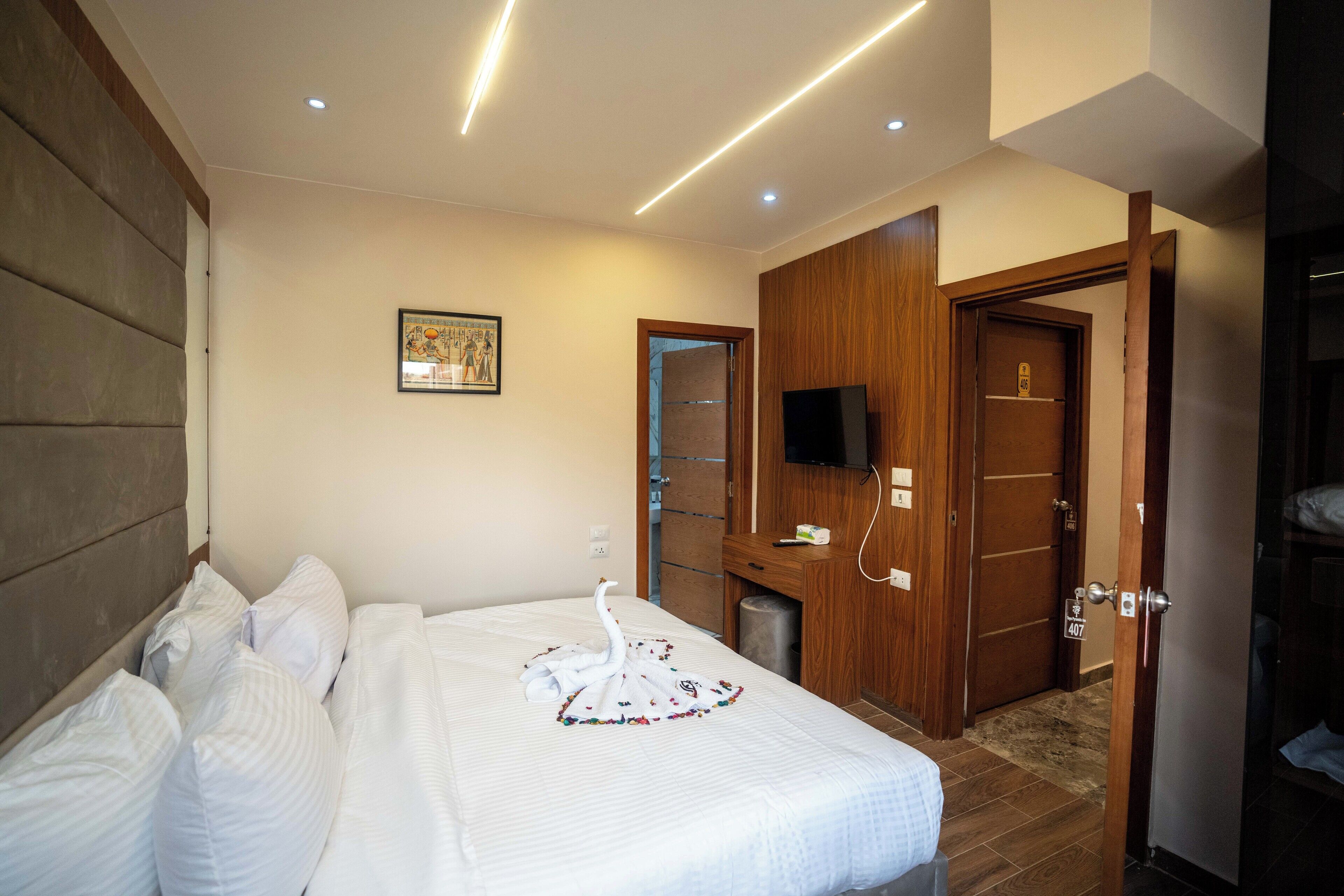 A hotel room with a neatly made bed, a television, and a wooden wardrobe.