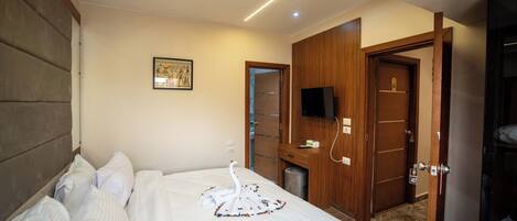 A hotel room with a neatly made bed, a television, and a wooden wardrobe.
