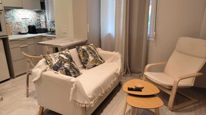 A cozy living area with a sofa, a chair, a small table, and a kitchen in the background.