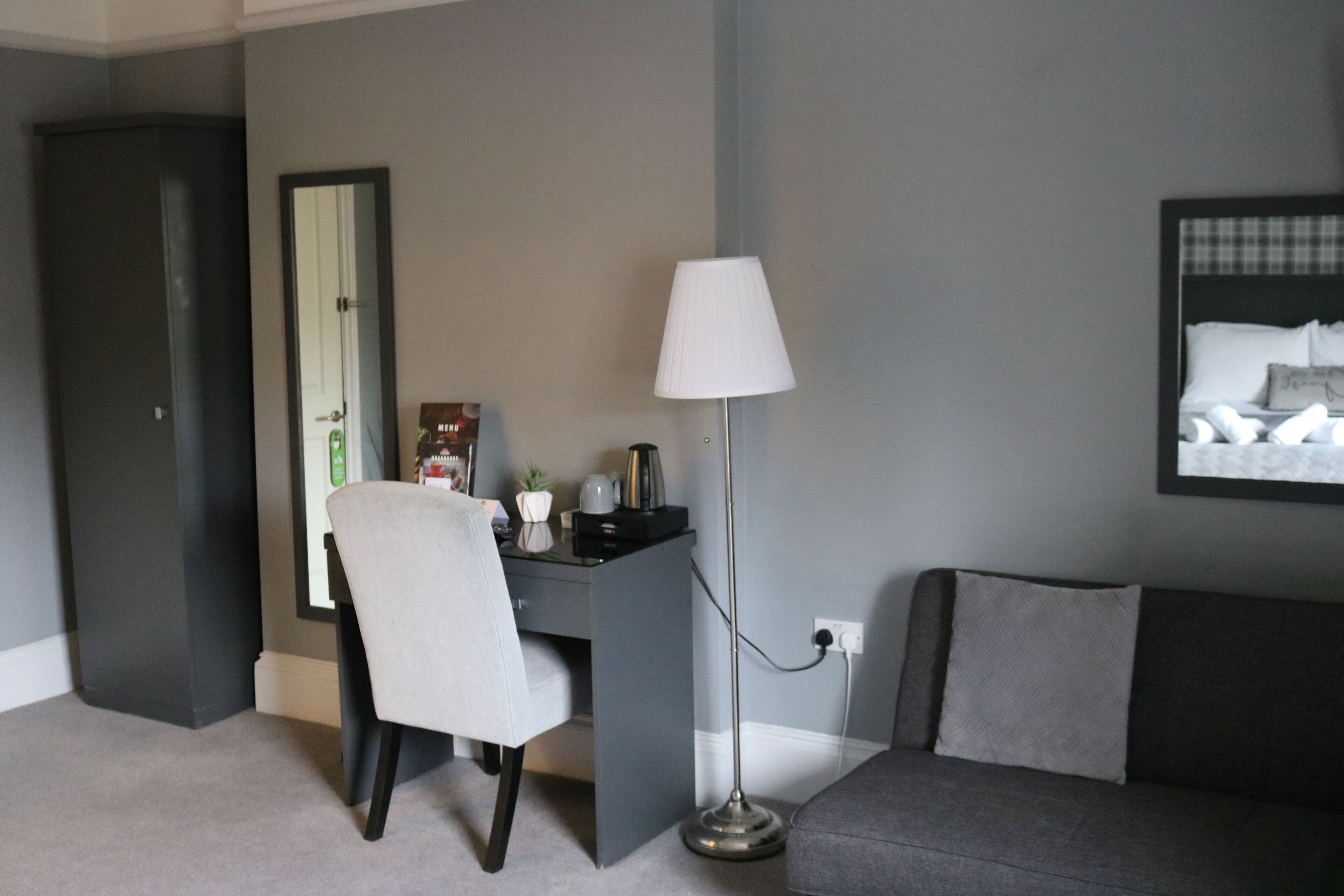 Une chambre à coucher moderne avec un bureau, une chaise, une lampe et un canapé gris.