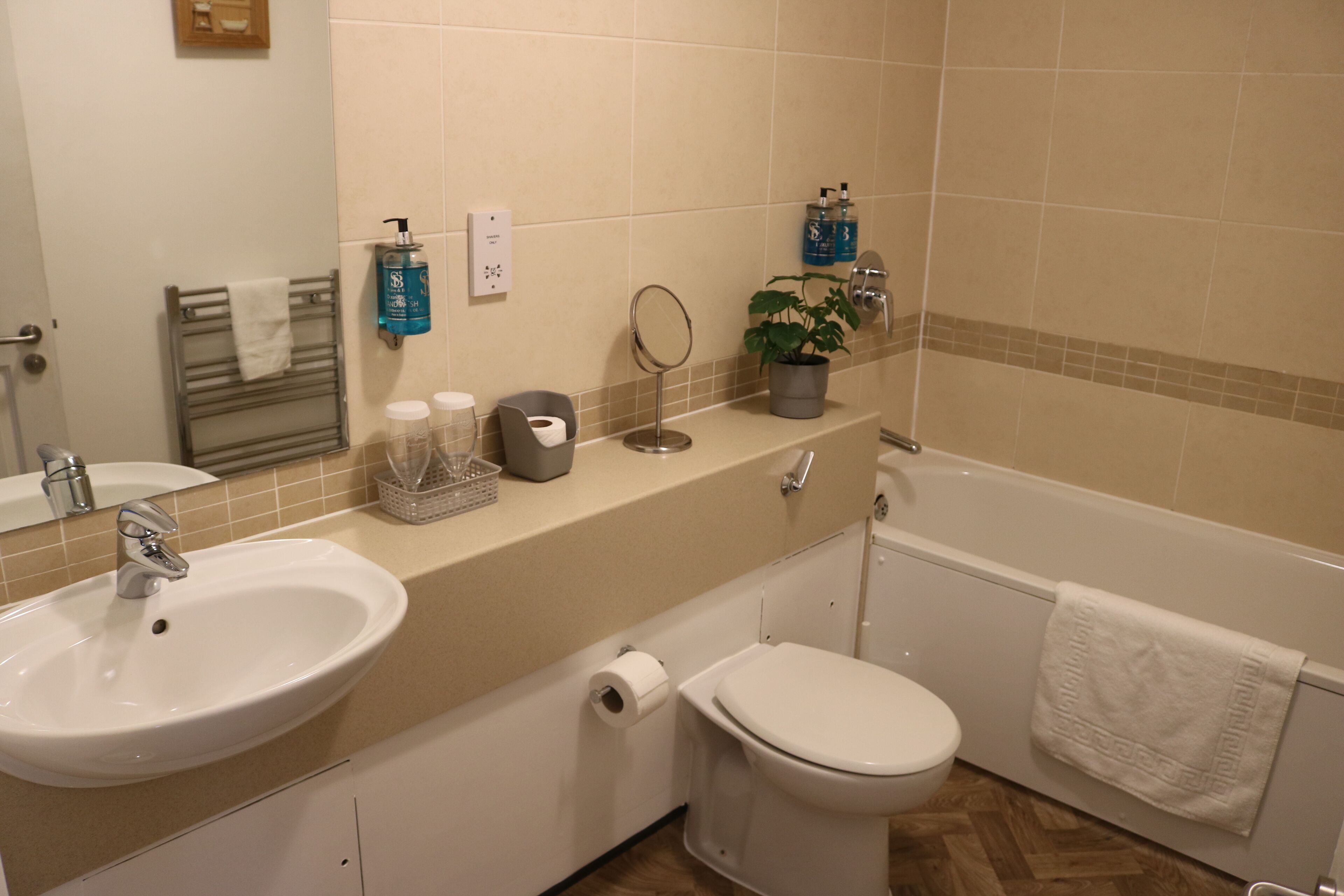 A bathroom with a sink, toilet, and bathtub. There are toiletries on the counter, a towel rack, and a mirror.
