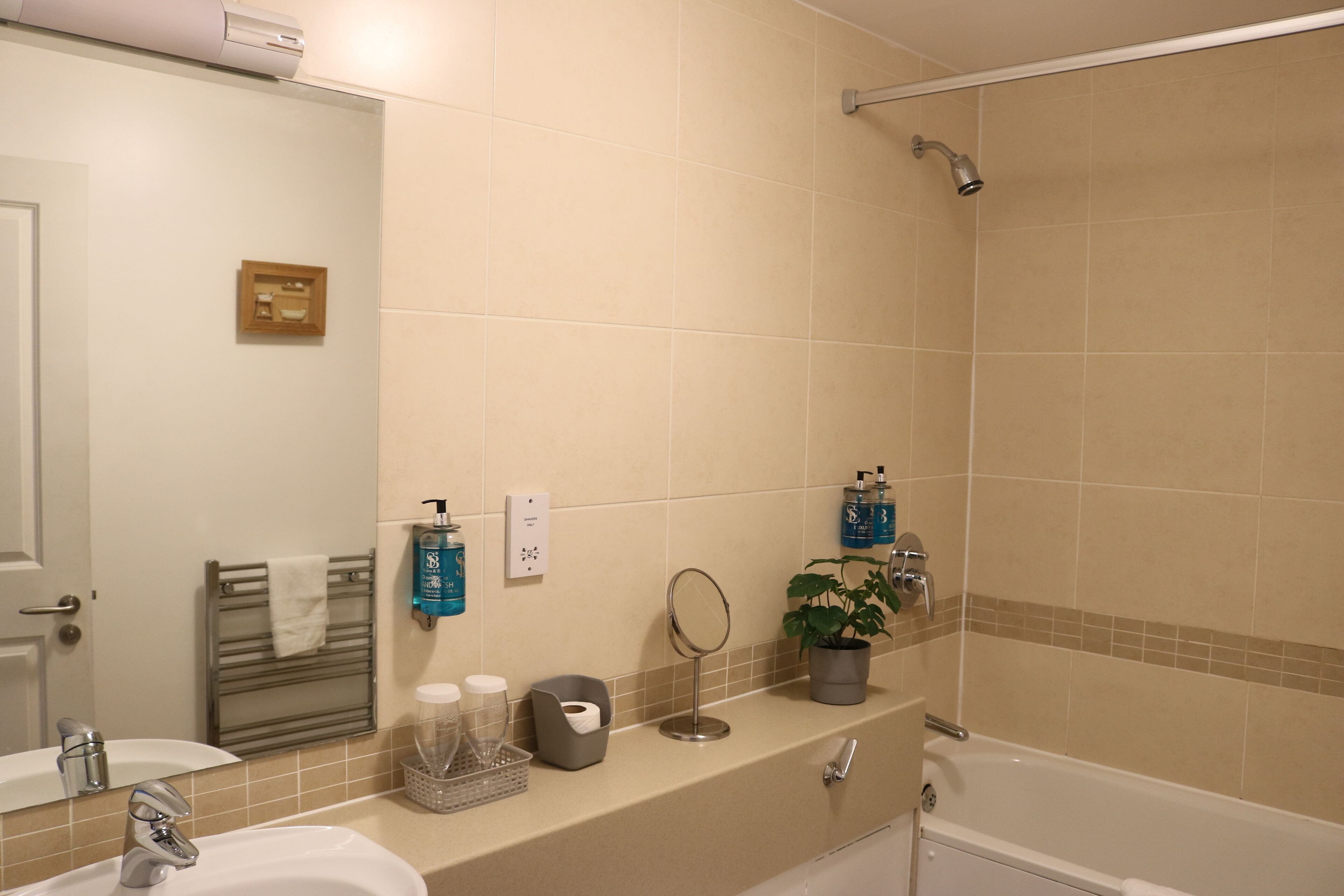 A bathroom with a sink, mirror, towel rack, shower, and toiletries on the countertop.