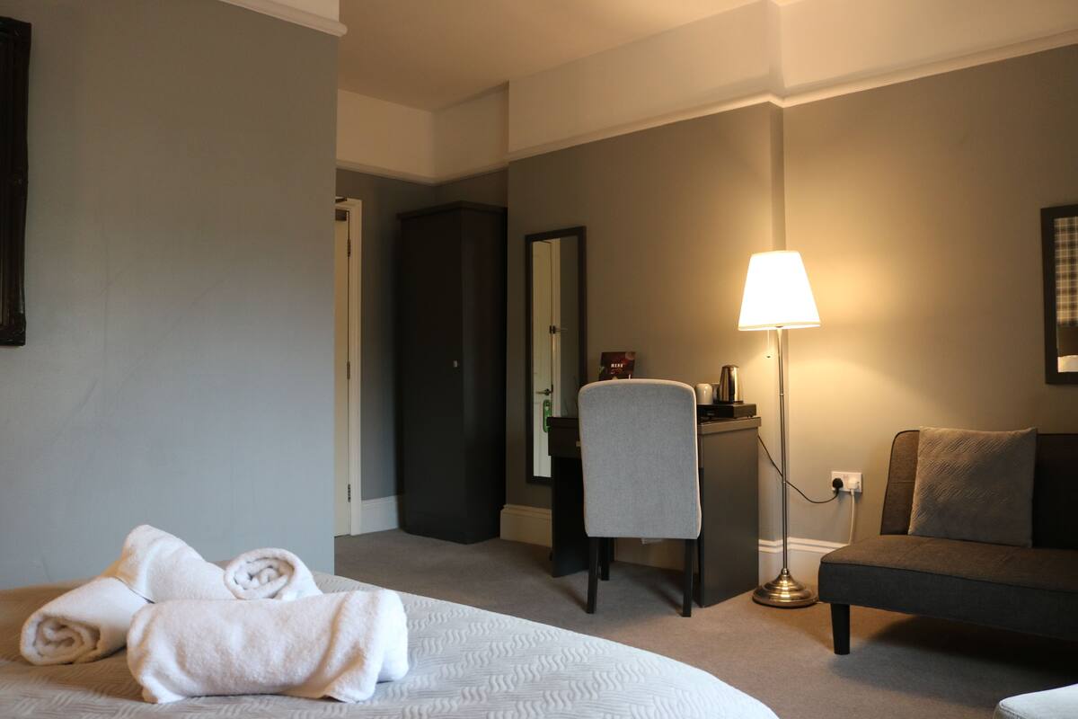 A hotel room with a bed, a desk, a chair, a lamp, and a sofa.