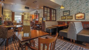 A restaurant with wooden tables, cushioned seating, and patterned wallpaper. - Norfolk Arms Hotel (Glossop)