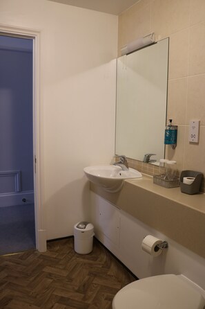 A bathroom with a sink, mirror, toilet, and trash can. - Norfolk Arms Hotel (Glossop)